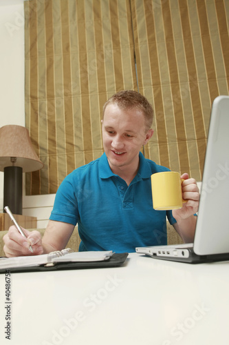 Photo: Man writing on organizer while holding a cup Man writing on organizer while holding a cup
