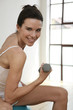 Woman sitting on fitness ball, lifting dumbbell