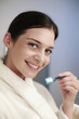 Woman in bathrobe holding toothbrush with toothpaste on it