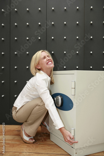 Photo: Businesswoman trying to lift safe Businesswoman trying to lift safe