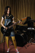 Young woman singing while playing guitar, man playing drums in the background