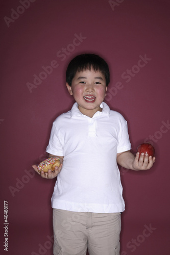 Foto: Boy holding doughnut and apple in each hand Boy holding doughnut and apple in each hand