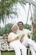 Foto: Senior couple smiling at the camera while sitting on a swing Senior couple smiling at the camera while sitting on a swing