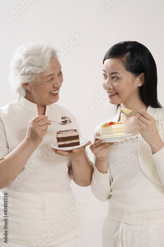Photo: Senior woman and woman smiling at each other while enjoying their cakes Senior woman and woman smiling at each other while enjoying their cakes