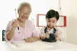 Foto: Senior woman writing calligraphy, boy helping her with the calligraphy ink stick Senior woman writing calligraphy, boy helping her with the calligraphy ink stick