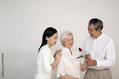 Photo: Senior man giving senior woman a stalk of rose, woman smiling while watching Senior man giving senior woman a stalk of rose, woman smiling while watching