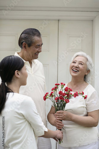 Photo: Woman giving senior woman a bouquet of flowers, senior man smiling while watching Woman giving senior woman a bouquet of flowers, senior man smiling while watching