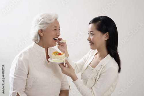 Photo: Woman feeding senior woman a slice of cake Woman feeding senior woman a slice of cake
