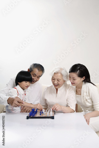 Photo: Boy playing chessgame with senior woman, woman and senior man watching Boy playing chessgame with senior woman, woman and senior man watching