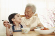 Photo: Senior woman helping boy to eat using with chopsticks Senior woman helping boy to eat using with chopsticks