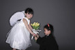 Boy with tuxedo and devil horns giving flowers to girl wearing white dress and angel wings