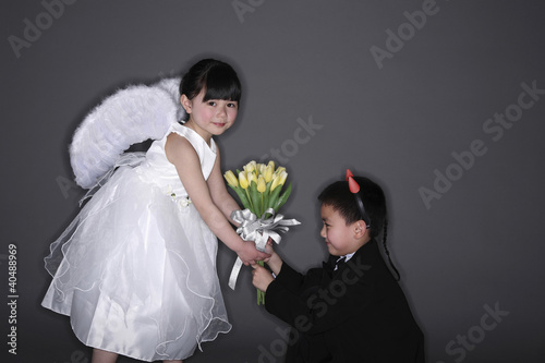 Photo: Boy with tuxedo and devil horns giving flowers to girl wearing white dress and angel wings Boy with tuxedo and devil horns giving flowers to girl wearing white dress and angel wings