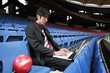 Businessman using laptop with football beside him on the stadium seat