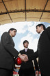 Businessmen shaking hands with another businessman watching in the background