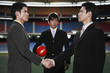 Businessmen shaking hands with another businessman watching in the background