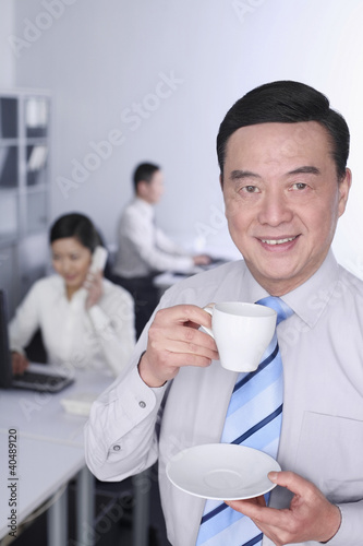 Foto: Businessman enjoying coffee with other business people are working in the background Businessman enjoying coffee with other business people are working in the background