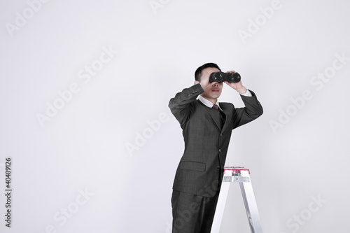 Foto: Businessman on ladder, looking through binoculars Businessman on ladder, looking through binoculars