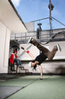 Photo: Young woman doing a breakdance move, young man with headphones using laptop in the background Young woman doing a breakdance move, young man with headphones using laptop in the background