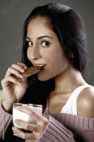 Photo: Woman biting on a cookie and holding a glass of milk Woman biting on a cookie and holding a glass of milk