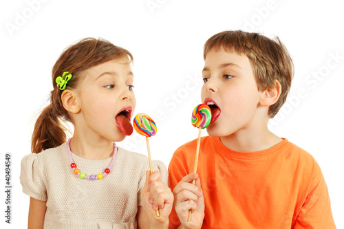 Photo: Happy brother and sister lick colorful lollipops isolated Happy brother and sister lick colorful lollipops isolated