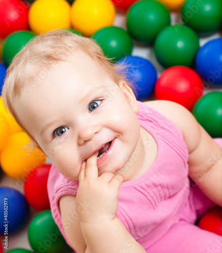 Photo: Portrait of a smiling infant playing among colorful balls Portrait of a smiling infant playing among colorful balls