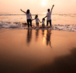 Photo: happy family holding hands on beach and watching the sunset happy family holding hands on beach and watching the sunset