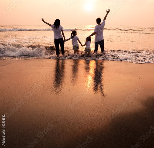 Photo: happy family holding hands on beach and watching the sunset happy family holding hands on beach and watching the sunset
