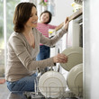 Girl watching her mother keeping the dishes in the dishwasher