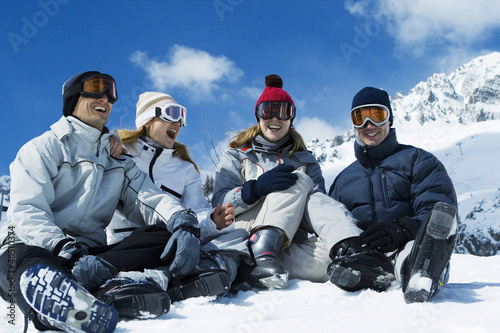 Photo: Friends sitting on snowy ground, laughing happily Friends sitting on snowy ground, laughing happily