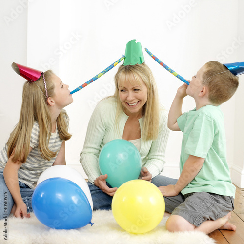 Photo: Boy and girl blowing party horn blowers, woman holding balloon Boy and girl blowing party horn blowers, woman holding balloon