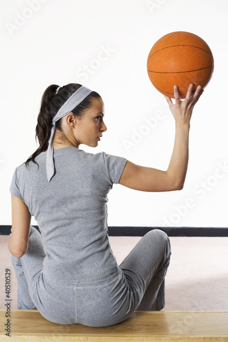 Photo: Woman sitting on bench holding up basketball Woman sitting on bench holding up basketball