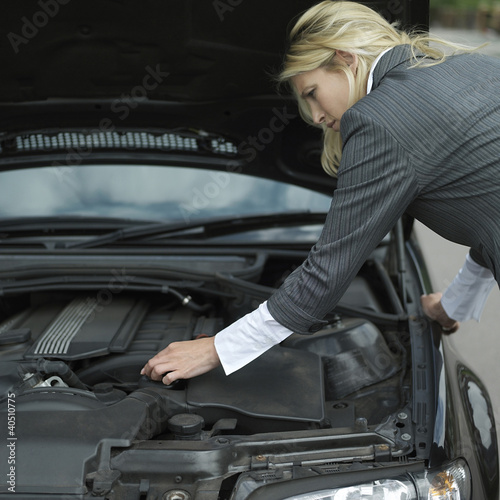 Photo: Businesswoman looking under car hood Businesswoman looking under car hood