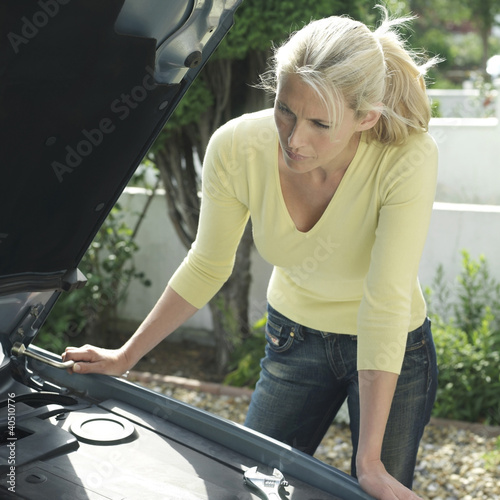 Photo: Woman with lug wrench looking under car hood Woman with lug wrench looking under car hood