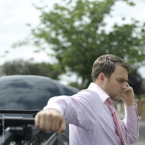 Photo: Businessman talking on the phone beside a broken down car Businessman talking on the phone beside a broken down car