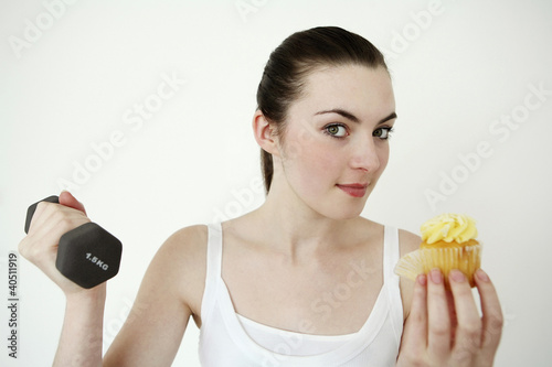 Photo: Woman eating cupcake while lifting dumbbell Woman eating cupcake while lifting dumbbell