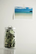 Photo: Bank notes in a transparent jar, picture of a beach hanging on the wall in the background Bank notes in a transparent jar, picture of a beach hanging on the wall in the background