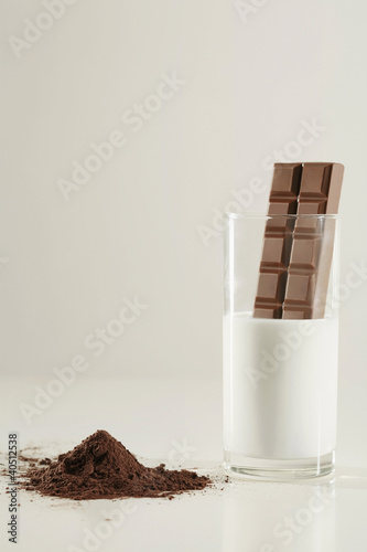 Photo: Chocolate bar dipping into a glass of milk, cocoa powder on the table Chocolate bar dipping into a glass of milk, cocoa powder on the table