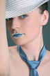 Woman with rhinestones on her lips wearing hat and necktie