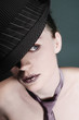 Woman with rhinestones on her lips wearing hat and necktie