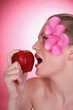 Woman with flower petals decorating her face, biting on a red apple
