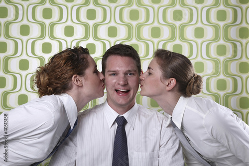 Photo: Two businesswomen kissing businessman on cheeks Two businesswomen kissing businessman on cheeks