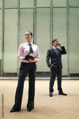 Photo: Businesswoman writing on organizer, businessman talking on the phone Businesswoman writing on organizer, businessman talking on the phone