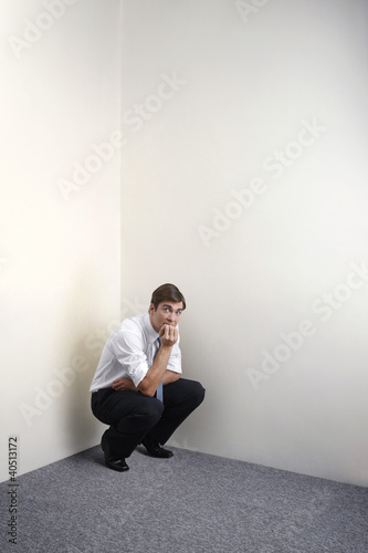 Foto: Businessman squatting down in corner of room Businessman squatting down in corner of room