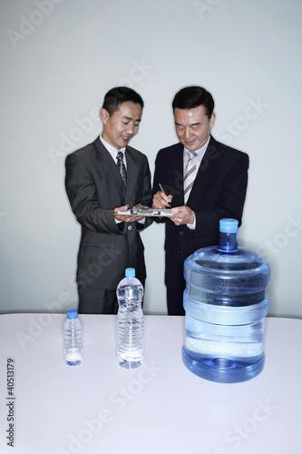 Photo: Businessman signing some documents held by his colleague Businessman signing some documents held by his colleague