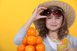 Little girl with pile of oranges wearing straw hat
