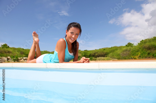 Photo: Brunette girl in fitness outfit relaxing by the pool Brunette girl in fitness outfit relaxing by the pool