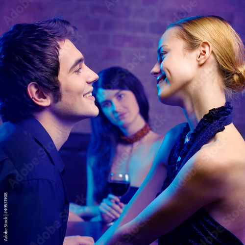 Photo: Young couple and woman looking at them at club Young couple and woman looking at them at club