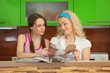Two girlfriends with women's magazines on kitchen Two girlfriends with women's magazines on kitchen