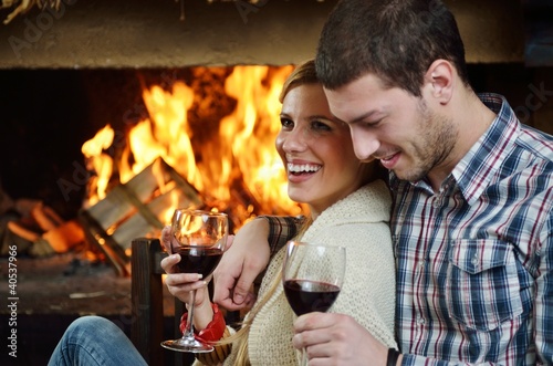 Photo: Young romantic couple sitting on sofa in front of fireplace at h Young romantic couple sitting on sofa in front of fireplace at h