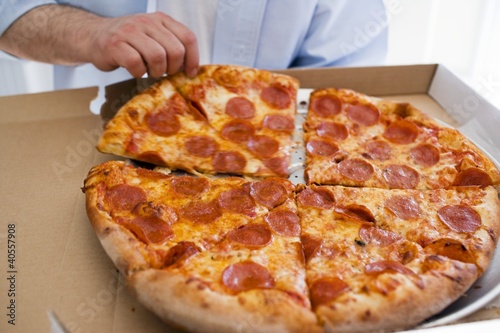 Photo: Hand taking piece of pepperoni pizza out of pizza box Hand taking piece of pepperoni pizza out of pizza box